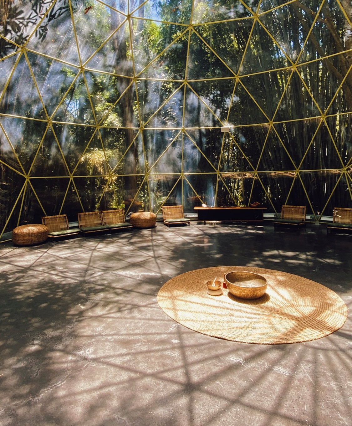 Inside the dome, brass struts triangulating the roof over a round jute mat set with singing bowls, cane chairs and woven floor cushions ringing the perimeter and bamboo shadows striping the polished concrete.